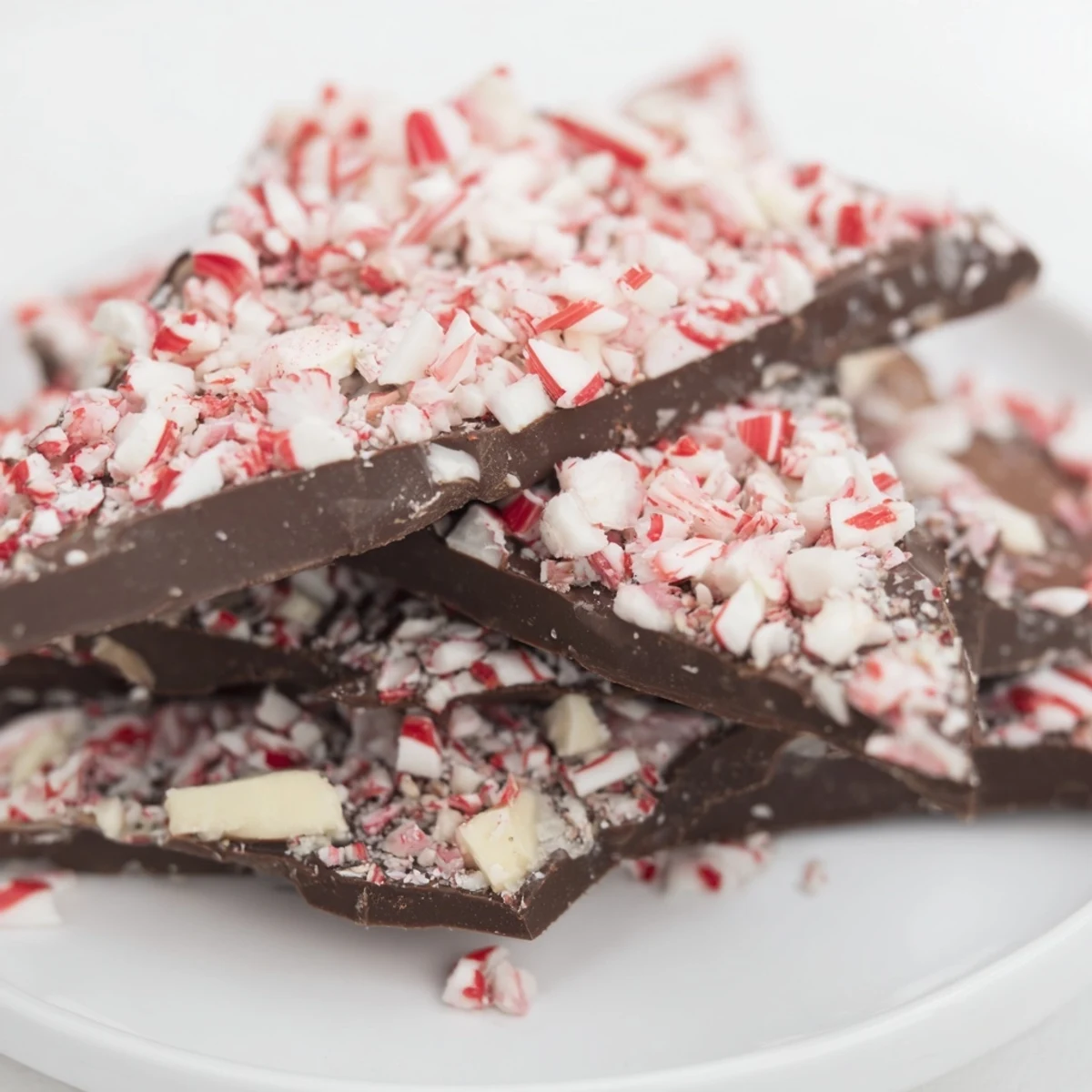 Golden holiday lights glow behind these Chocolate Peppermint Bark Shards, showcasing smooth chocolate textures and vibrant red mint crumbles.