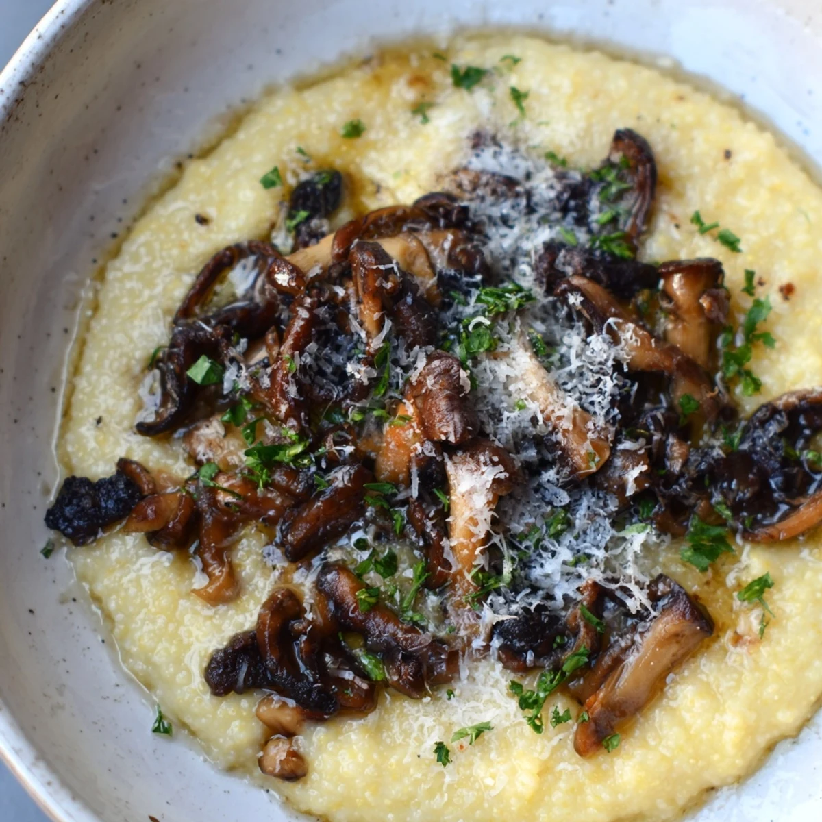 Creamy polenta with roasted mushrooms, topped with fresh parsley and grated Parmesan, served steaming in a rustic ceramic bowl.