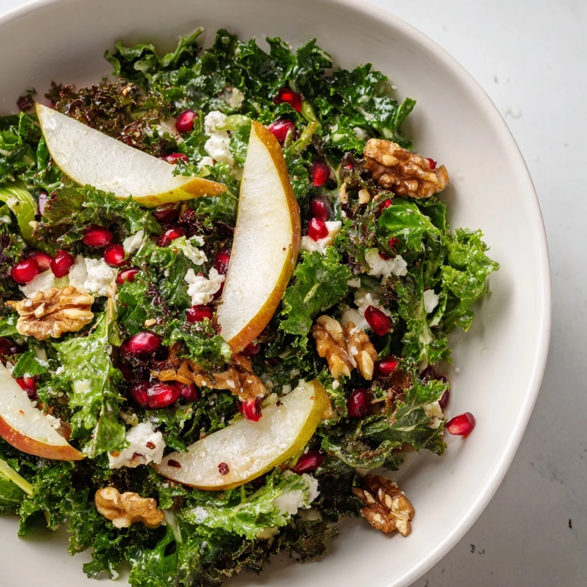 Healthy Winter Green Salad with Pear and Walnuts served in a white bowl with fresh kale and arugula, ready to eat.