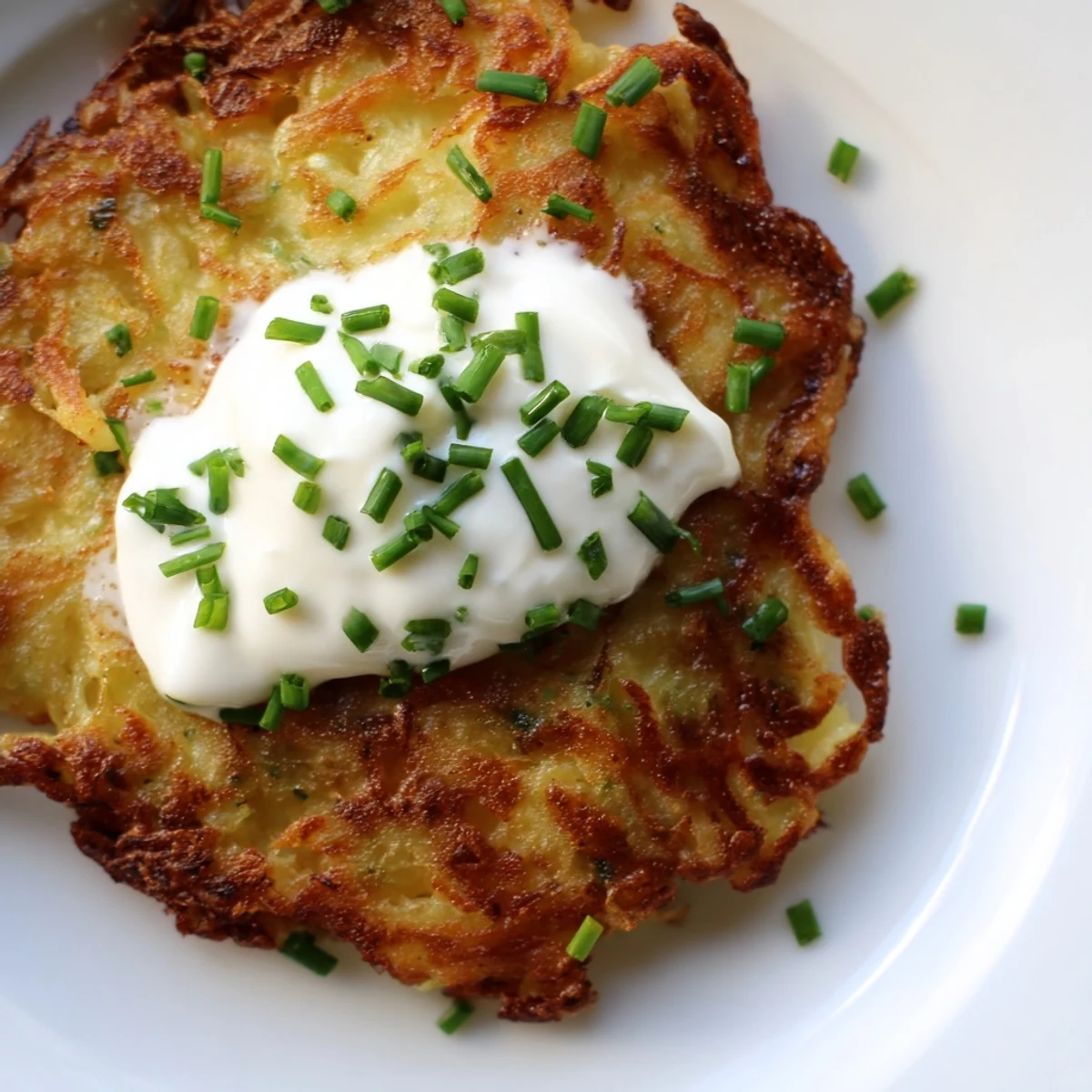 Golden-brown Irish Boxty potato pancakes sizzling in a skillet, ready to be topped with a dollop of cool sour cream.  
