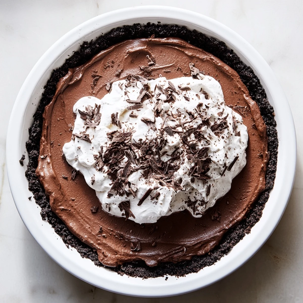 Freshly whipped cream and dark chocolate shavings top a chilled slice of Romantic Chocolate Silk Pie, revealing its velvety, rich filling inside the crunchy crust.