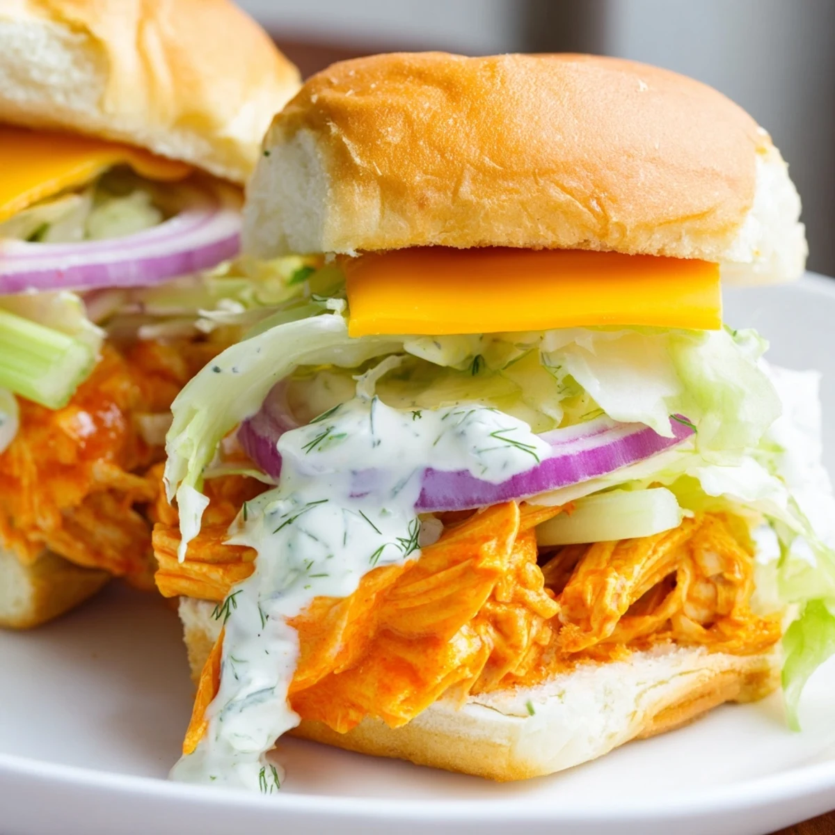 Buffalo chicken sliders with ranch, shredded lettuce, red onion, and celery on buttery slider buns.