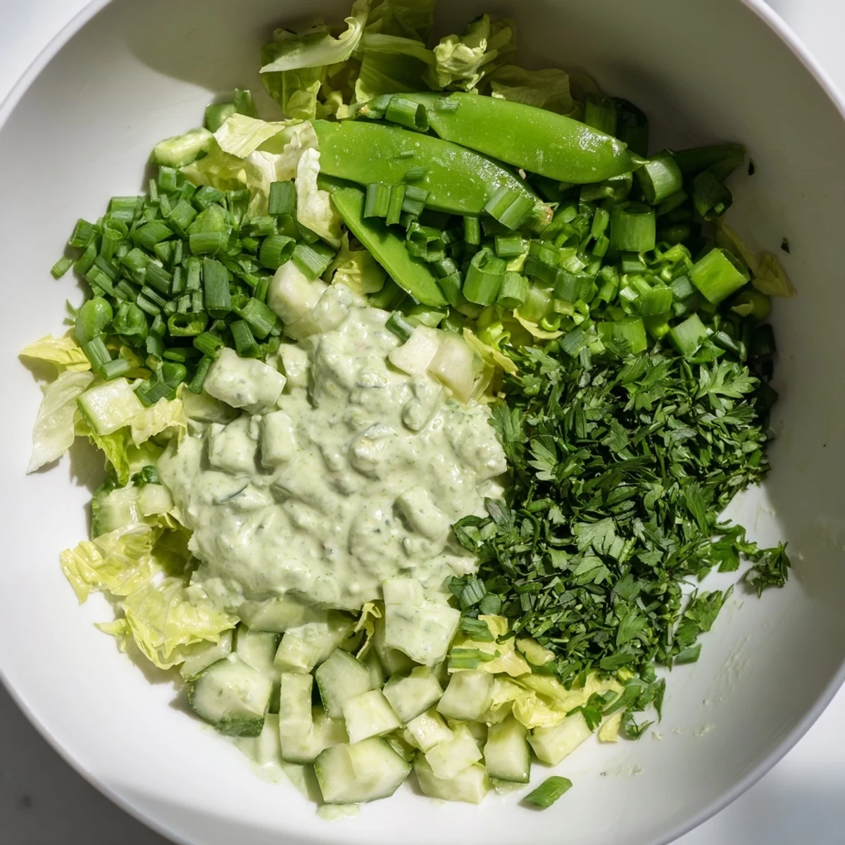Bright green Green Goddess Salad in a white bowl, showcasing crisp cucumber, creamy avocado, and fresh herbs.
