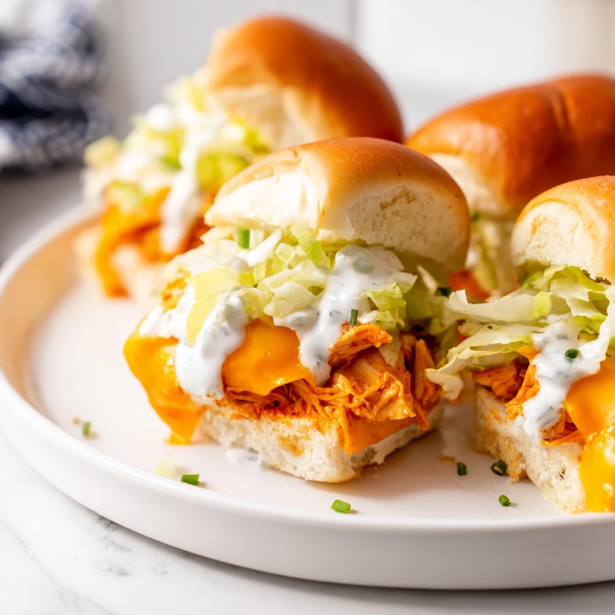 Golden-baked Buffalo Chicken Sliders with ranch dressing and crisp lettuce on soft buns, served on a platter.