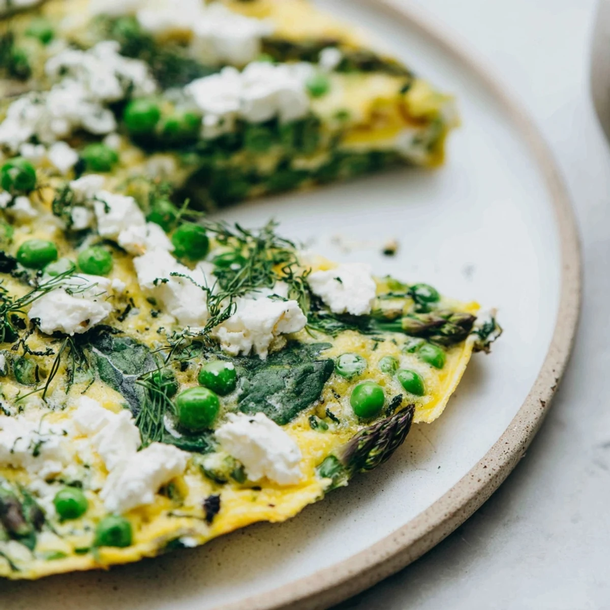 A close-up slice of Spring Vegetable Frittata with Goat Cheese and Herbs showing fluffy eggs, creamy crumbles, and chopped chives on a rustic plate.
