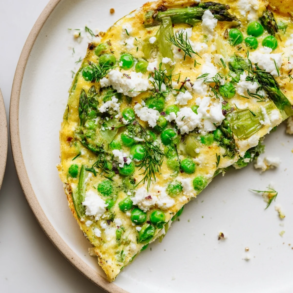 Plated Spring Vegetable Frittata with Goat Cheese and Herbs served beside a green salad and a glass of white wine for a light brunch.