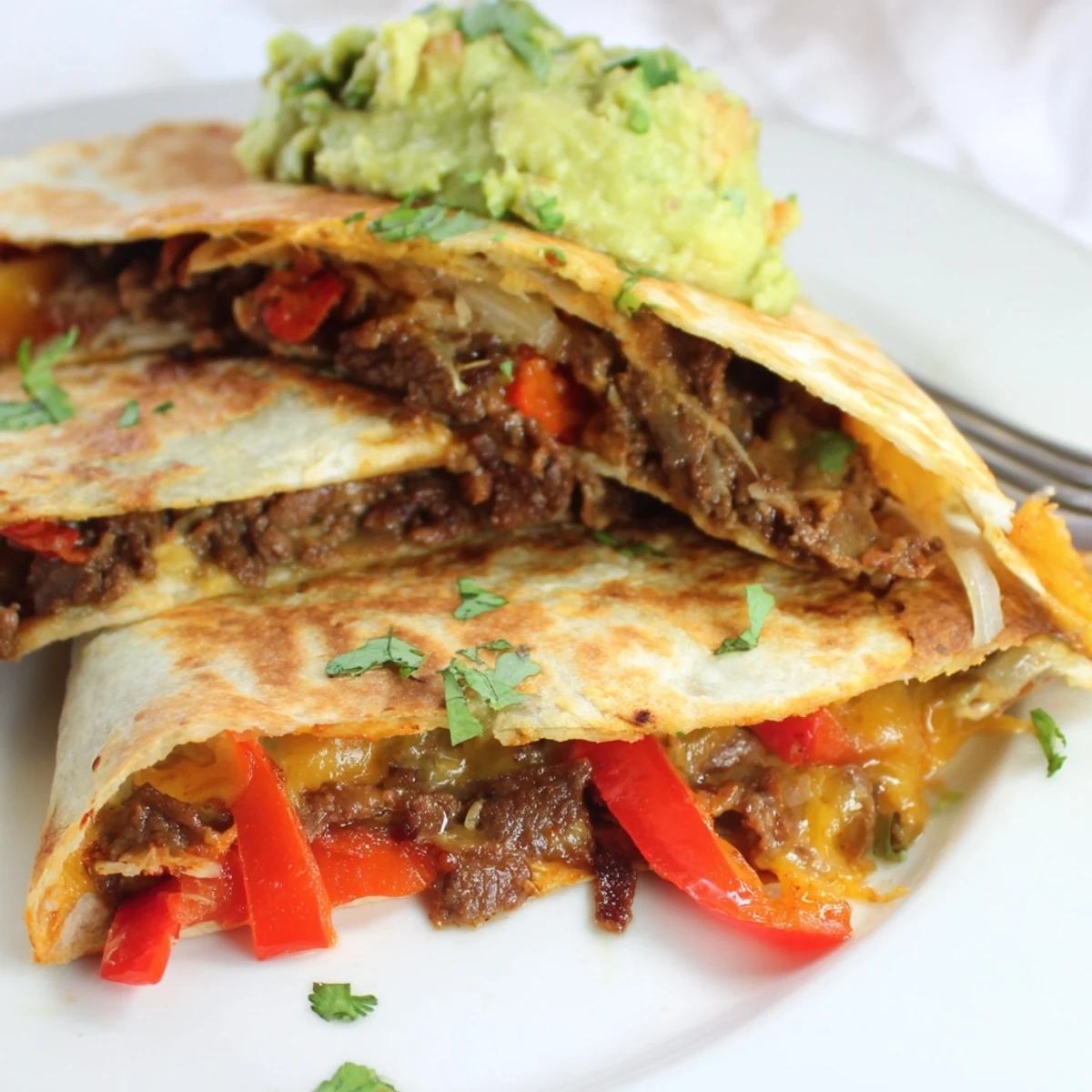 A close-up of crispy Beef Quesadillas with Salsa and Guacamole, showing the juicy beef and creamy dip beside lime wedges.