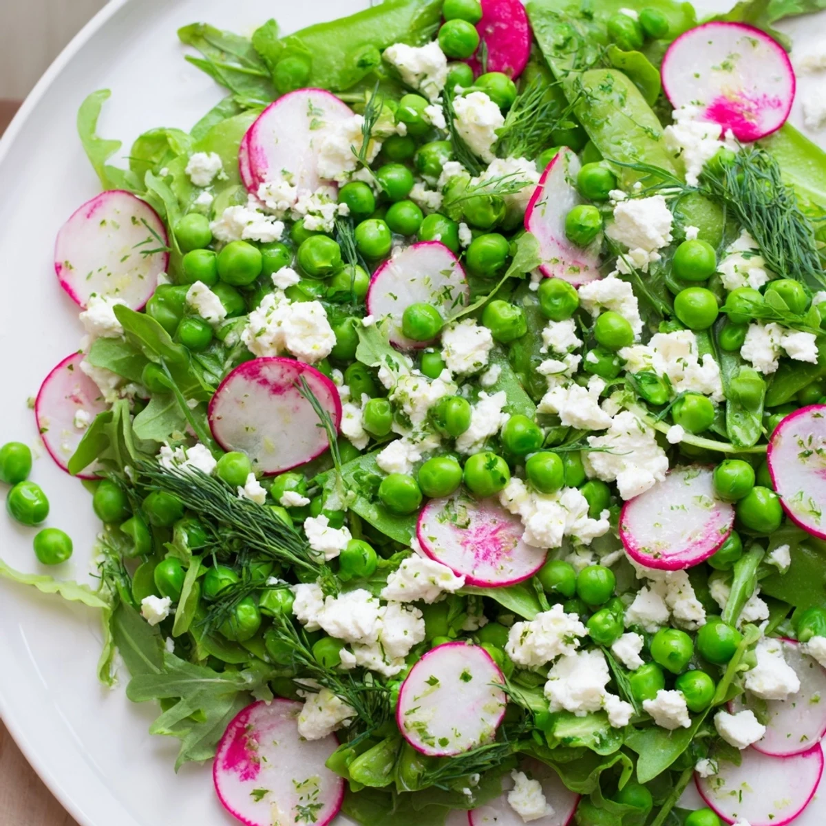 Colorful Spring Pea Salad with Radishes and Feta features creamy feta, crisp radishes, and bright peas beside a small lemon wedge.