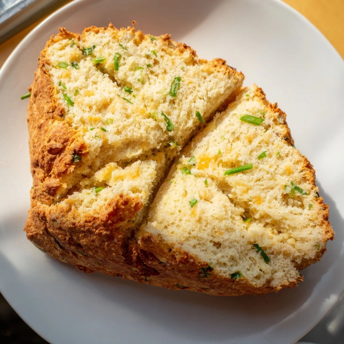 Warm slice of Savory Cheddar & Chive Irish Soda Bread on a wooden board, steam rising beside a cup of tomato soup for dipping.