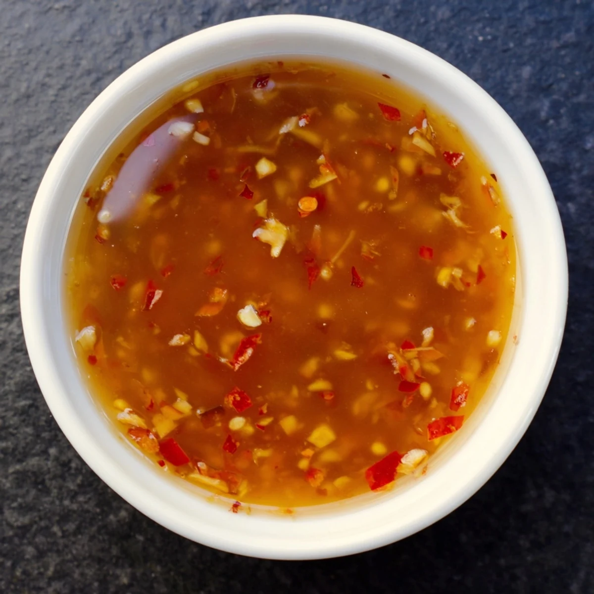 The Best Asian Coleslaw Dressing glistens with sesame oil and fresh ginger in a small glass jar.