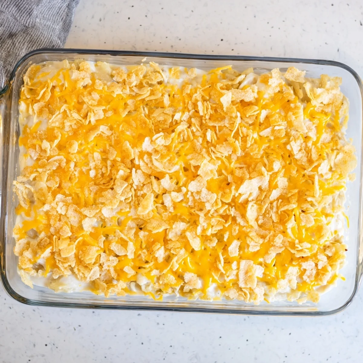 Funeral Potatoes with Hashbrowns baked golden with a buttery cornflake topping on a white ceramic plate.