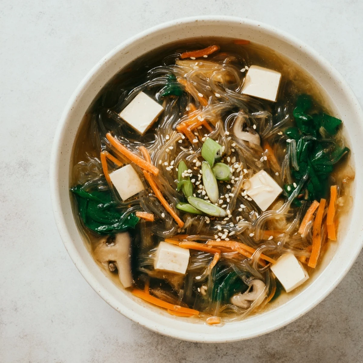 Steaming Japanese Harusame Noodle Soup served in a white bowl, garnished with spring onions and sesame seeds, showing tender tofu cubes and vibrant veggies.
