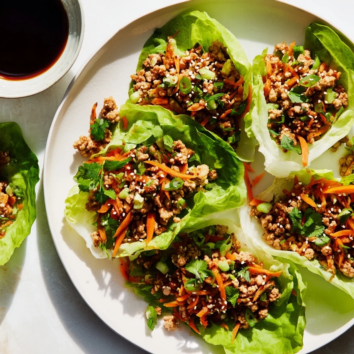 Potsticker Chicken Lettuce Boats arranged on a white plate with cilantro garnish and a side of dipping sauce for a light meal.