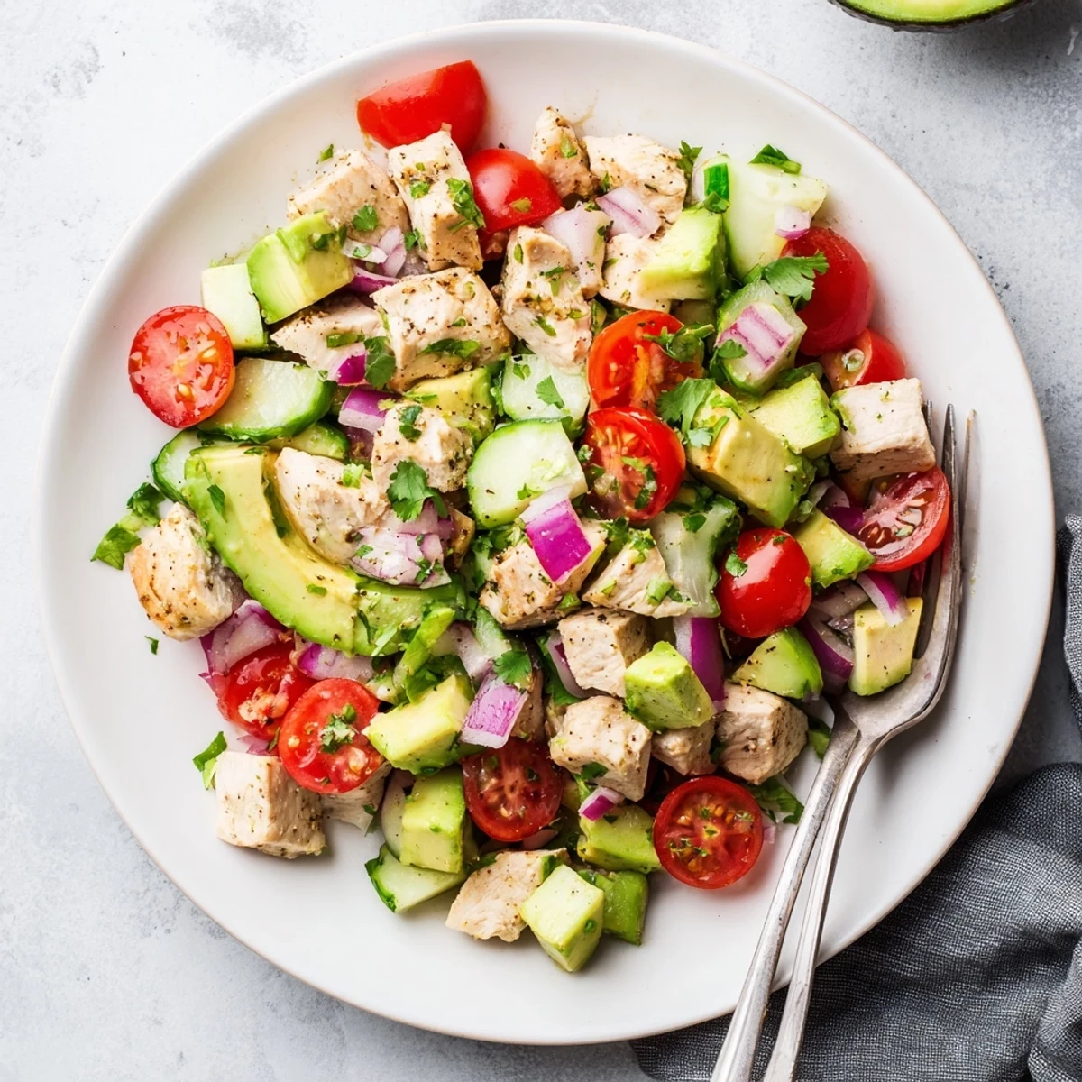 Creamy avocado chicken salad with grilled chicken, juicy tomatoes, and fresh cilantro on a rustic plate.