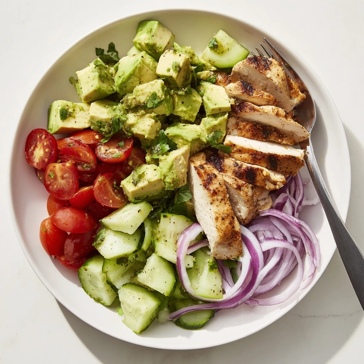 A close-up of creamy Avocado Chicken Salad with lime dressing, sliced red onion, and cilantro garnish on a white plate, ready to serve. 