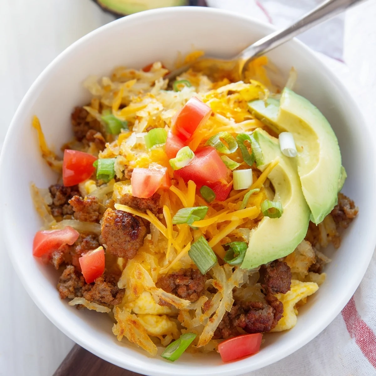 Crispy hash browns topped with fluffy eggs, savory sausage, and fresh avocado in a hearty breakfast bowl.