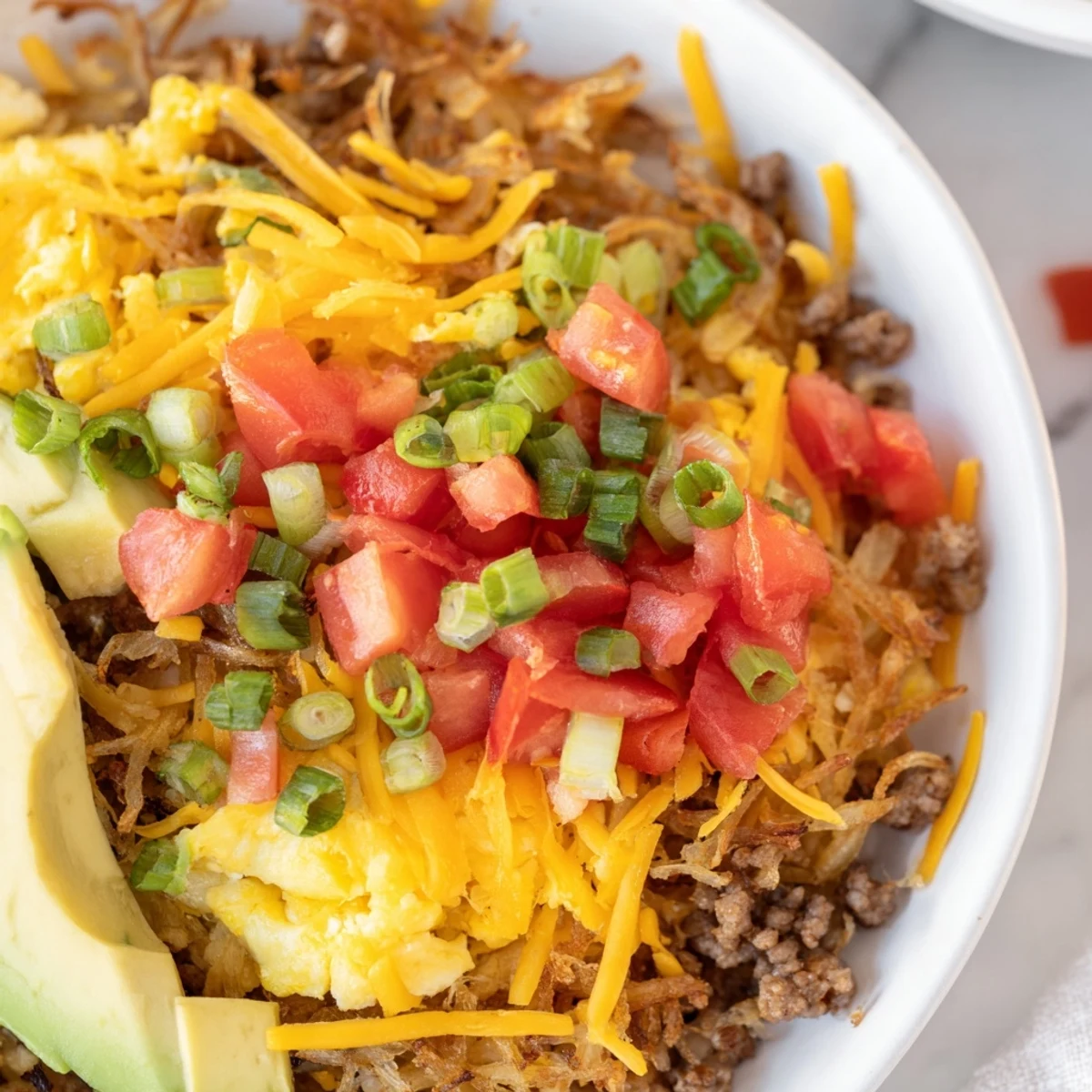 A steaming Hash Brown Breakfast Bowl with melted cheese, diced tomatoes, and a drizzle of hot sauce.