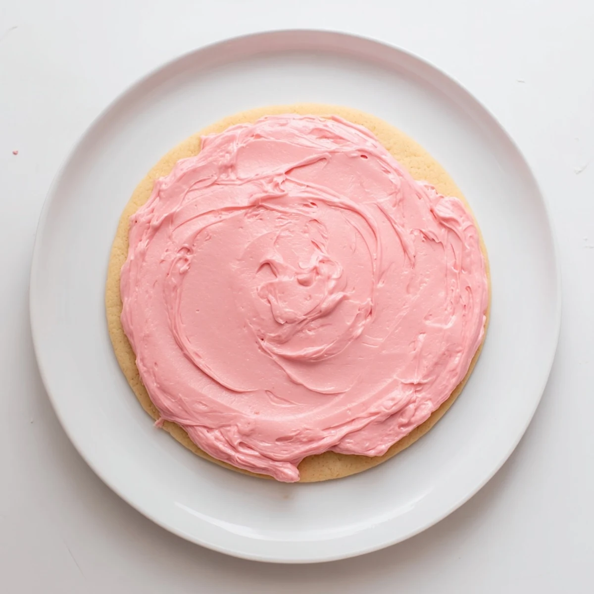 Golden Crumbl Pink Sugar Cookies cooling on a wire rack with vibrant pink almond frosting swirled on top.
