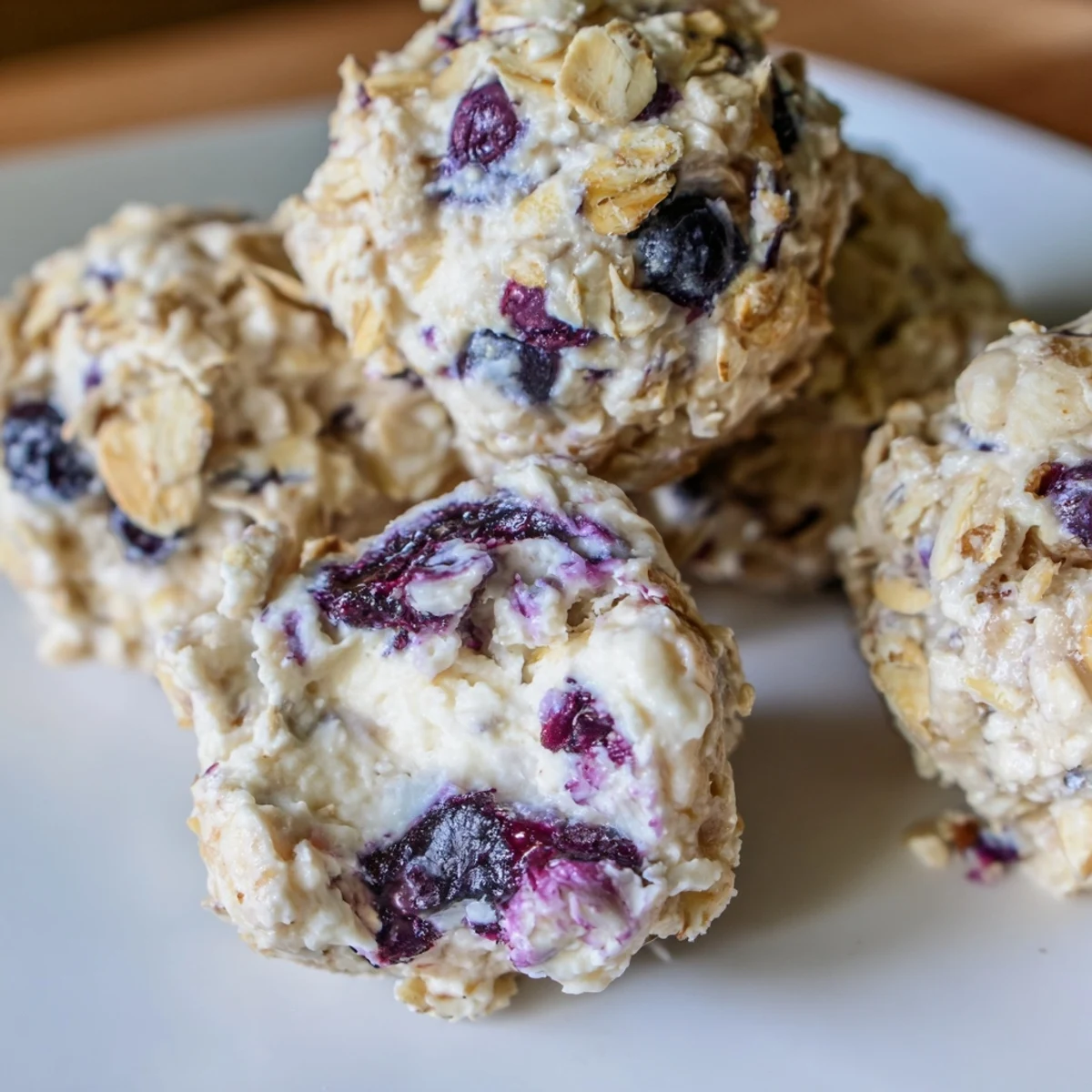Blueberry Cheesecake Protein Bites arranged on a marble tray with fresh blueberries and a dusting of powdered sugar, perfect for healthy snacking.