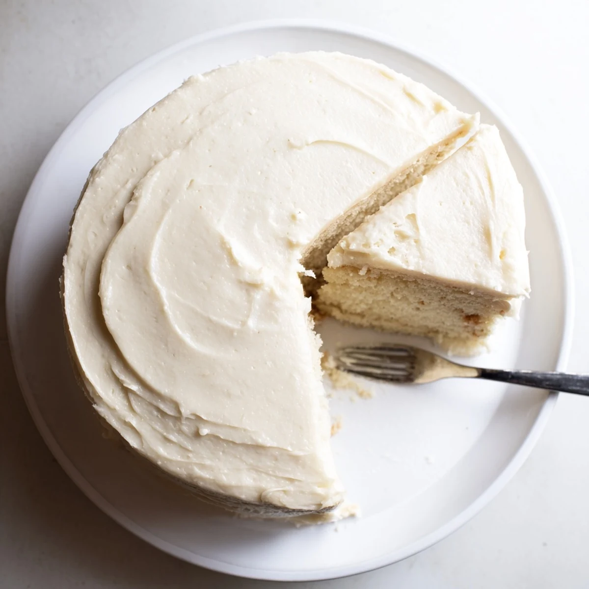 Perfect Vanilla Cake slice on a white plate showing soft crumb and fluffy vanilla buttercream frosting, ready to serve.