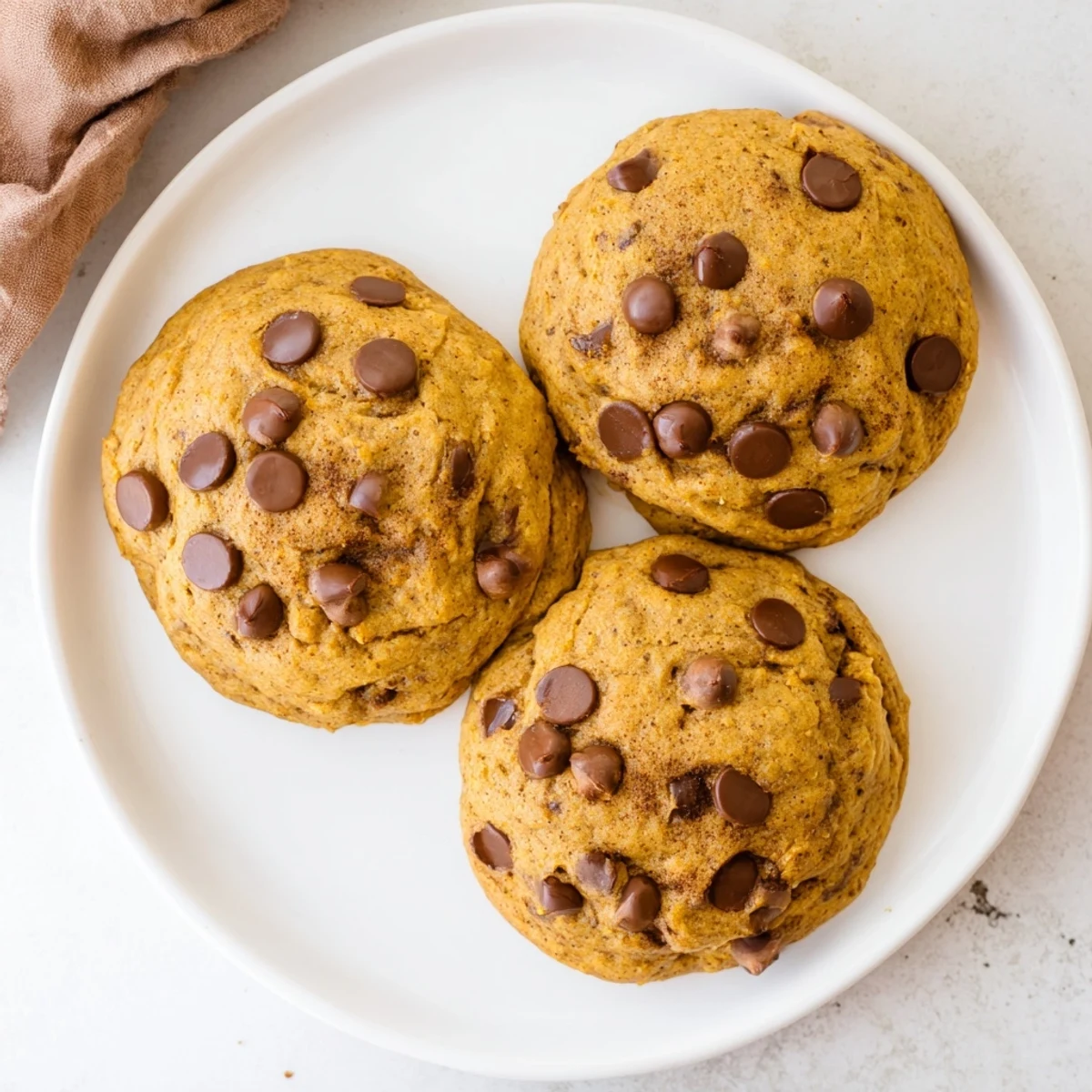 Soft chewy pumpkin spice chocolate chip cookies with melted chocolate chips on a white plate