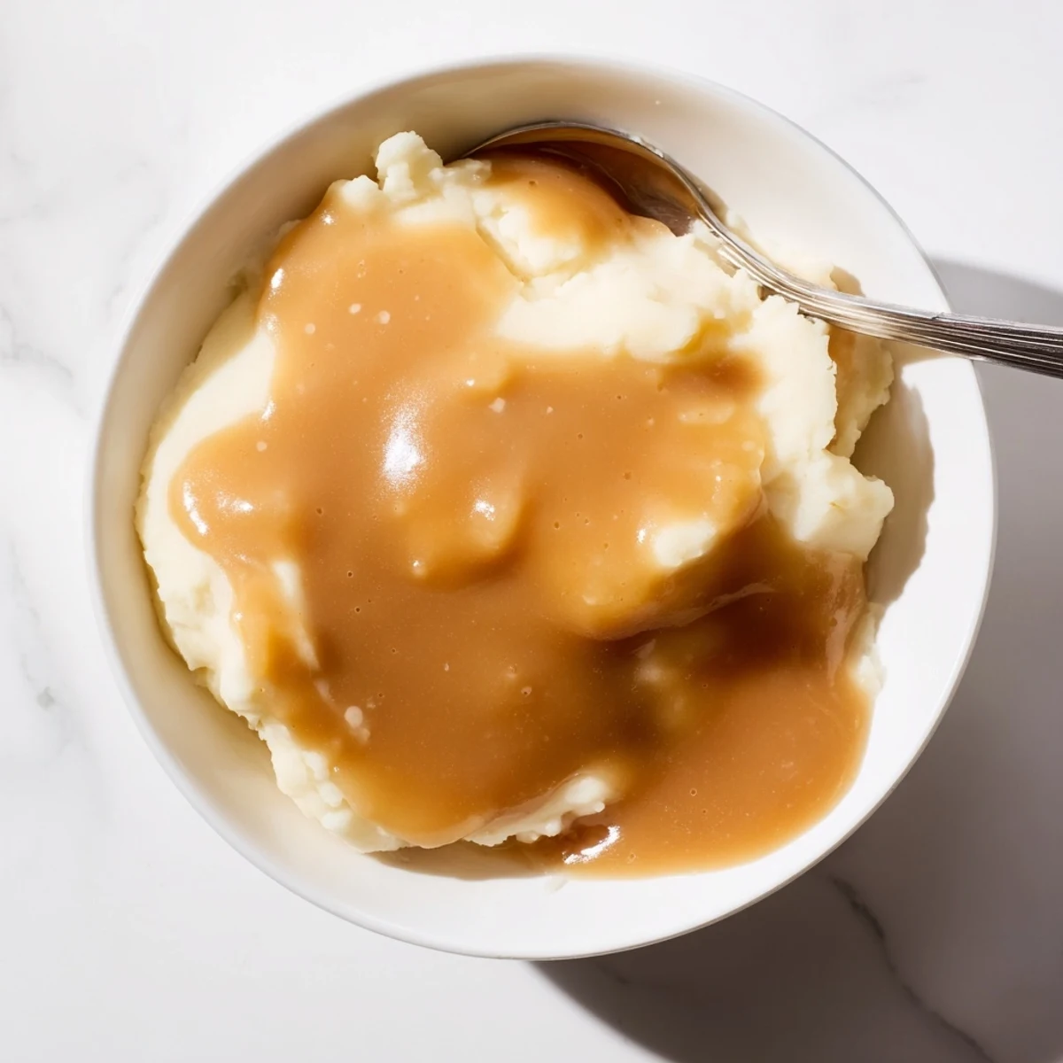 Silky smooth homemade gravy cascading down a heap of buttery mashed potatoes on a ceramic plate
