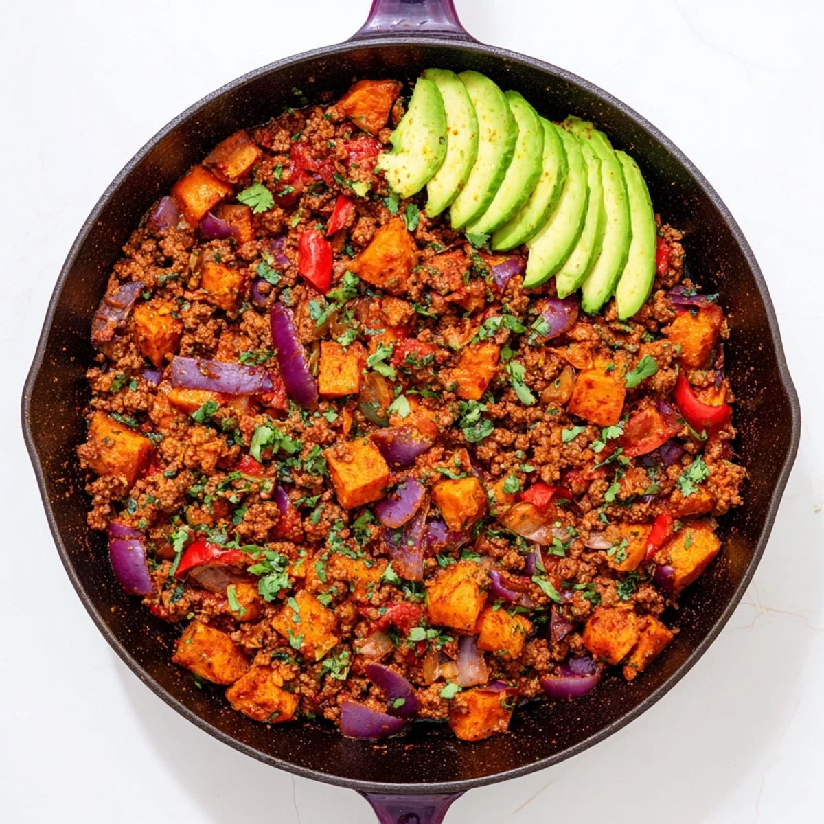 Hearty Southwest ground beef and sweet potato skillet topped with fresh cilantro and avocado