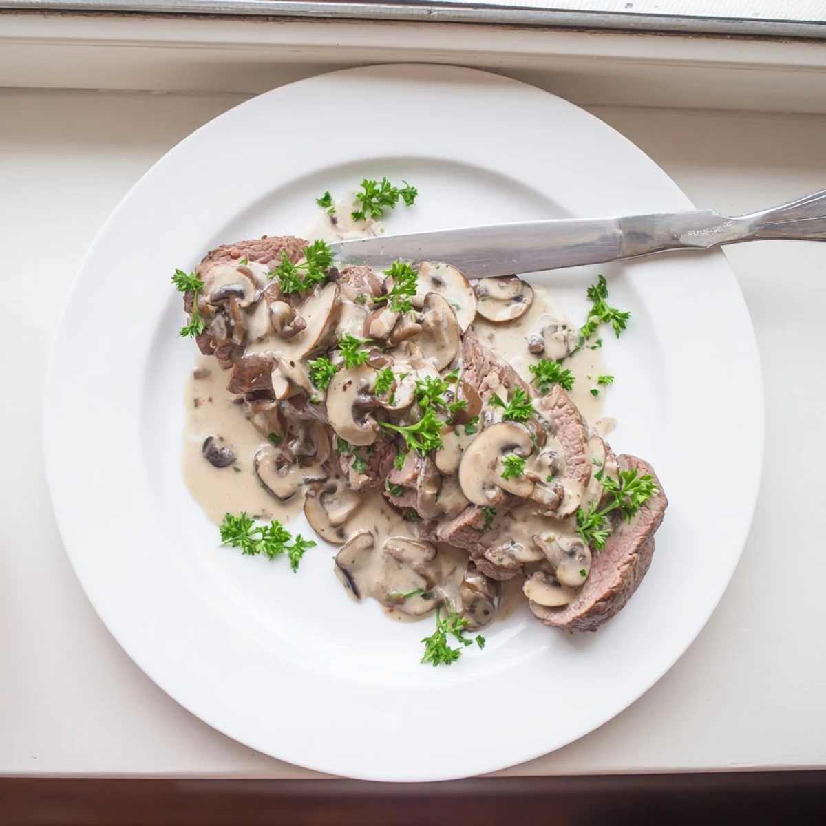 Golden seared beef tenderloin roast plated alongside rich creamy mushroom sauce