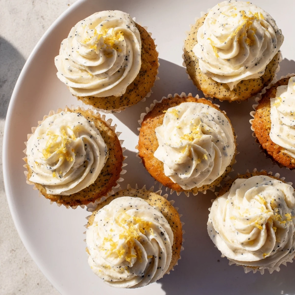Golden lemon poppy seed cupcakes topped with swirls of creamy lemon frosting on a white plate
