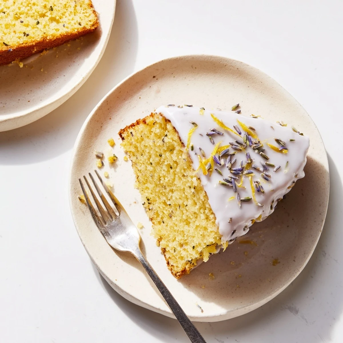 Golden lemon lavender cake drizzled with white glaze and sprinkled with purple lavender buds on a white plate