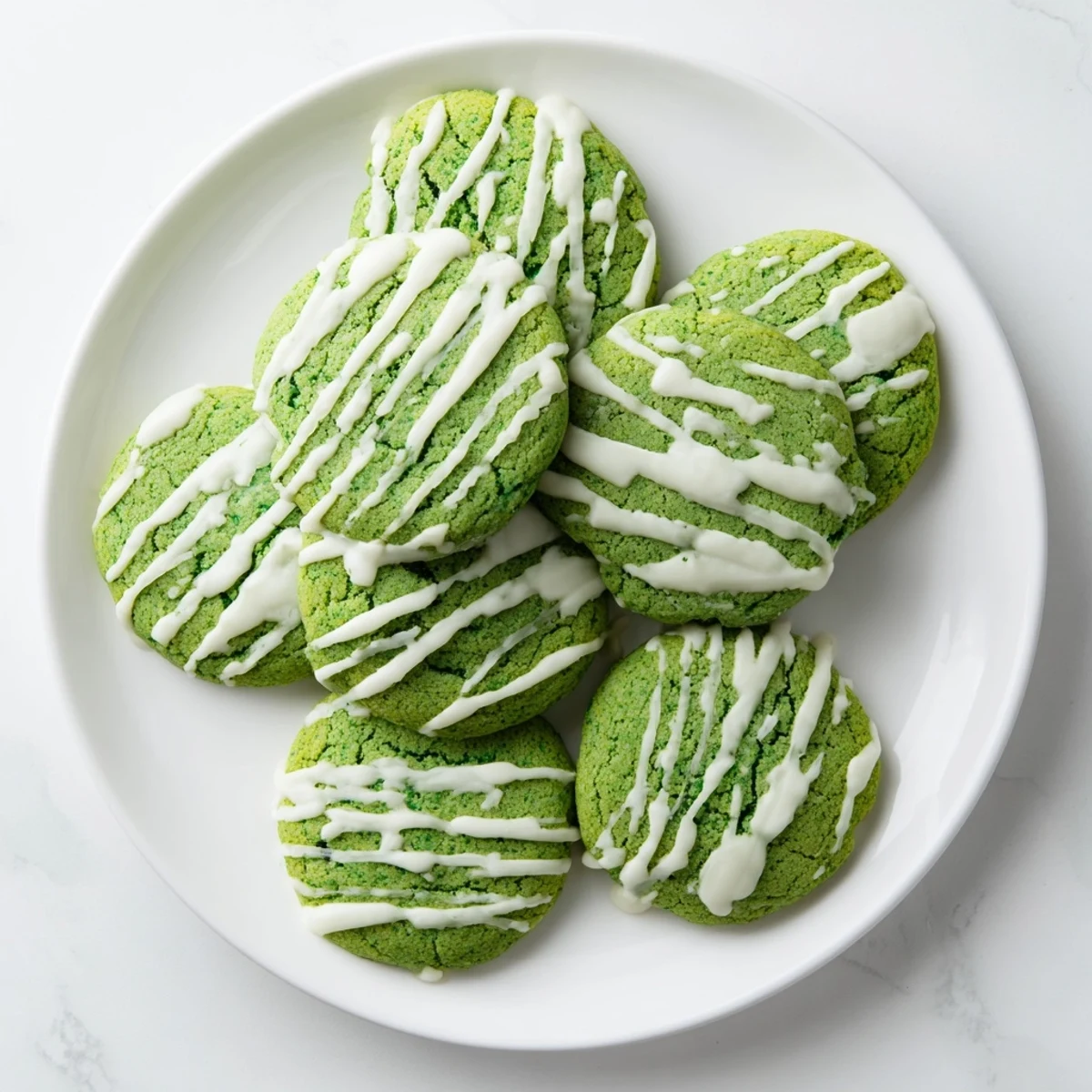 Soft green velvet cookies topped with melted white chocolate drizzle on a white plate