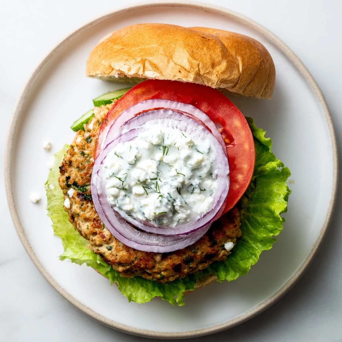 Golden grilled Greek chicken burgers topped with creamy homemade tzatziki sauce and fresh vegetables on toasted buns