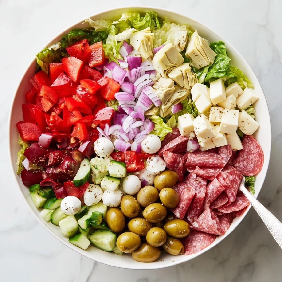 Colorful antipasti chopped salad bowl with fresh vegetables, olives, and Italian cheeses drizzled with herb dressing