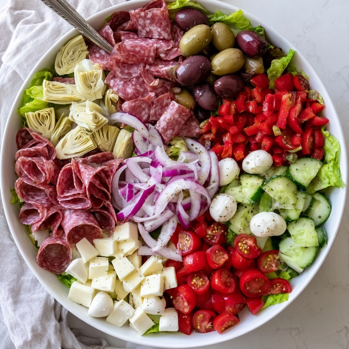 Vibrant Italian antipasti chopped salad featuring romaine, artichokes, salami, roasted peppers, and mozzarella balls