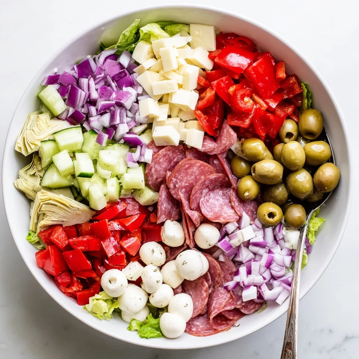 Fresh antipasti chopped salad with crisp vegetables, cured meats, and tangy pepperoncini in a large white bowl