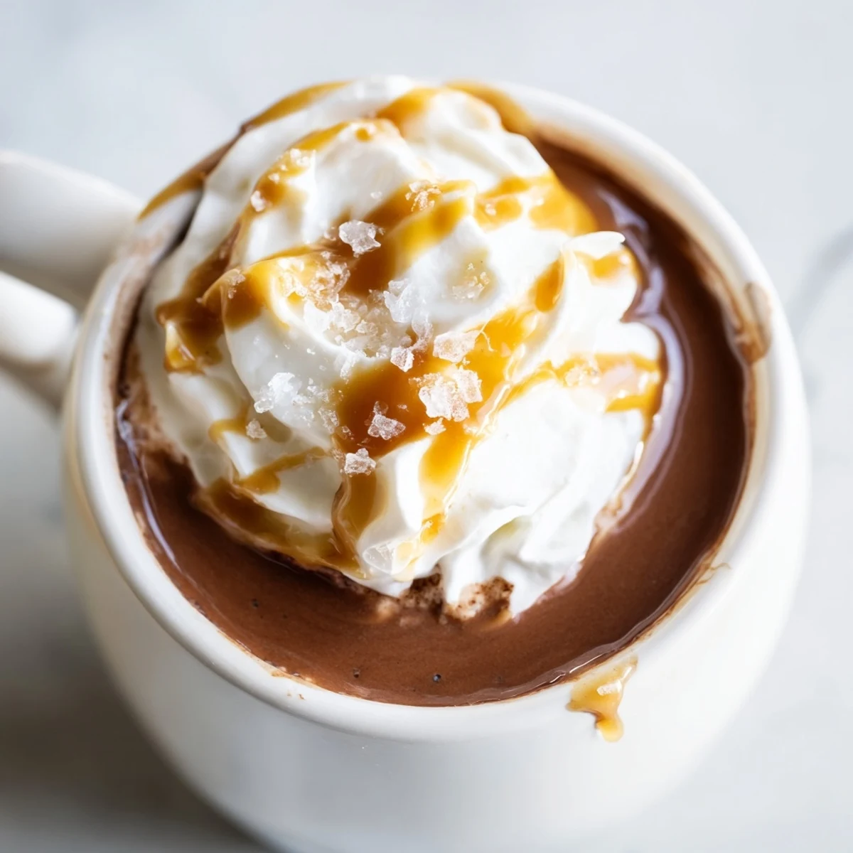 Creamy salted caramel hot chocolate topped with whipped cream and flaky sea salt garnish