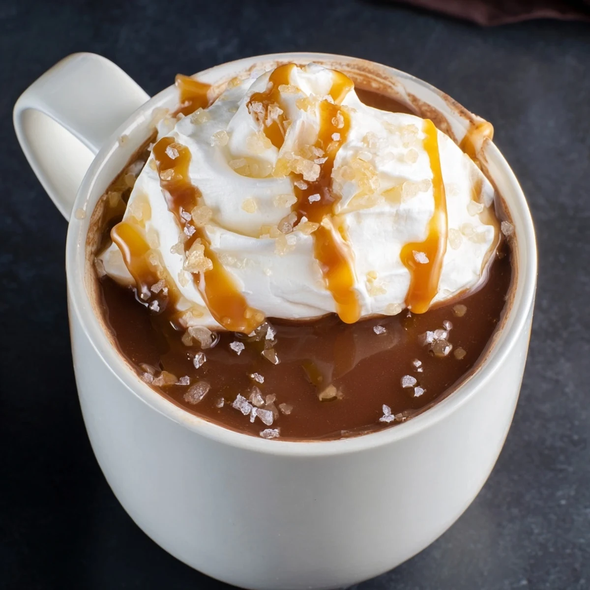 Two cozy mugs of salted caramel hot chocolate sprinkled with sea salt on wooden table