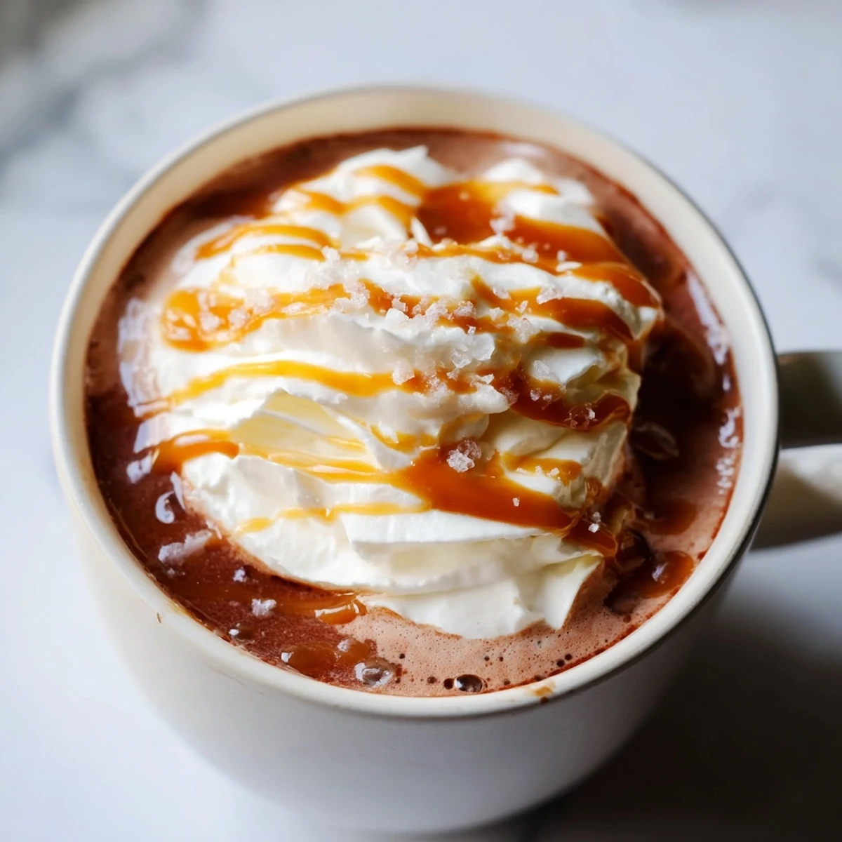 Steaming mug of rich salted caramel hot chocolate with caramel drizzle and white foam
