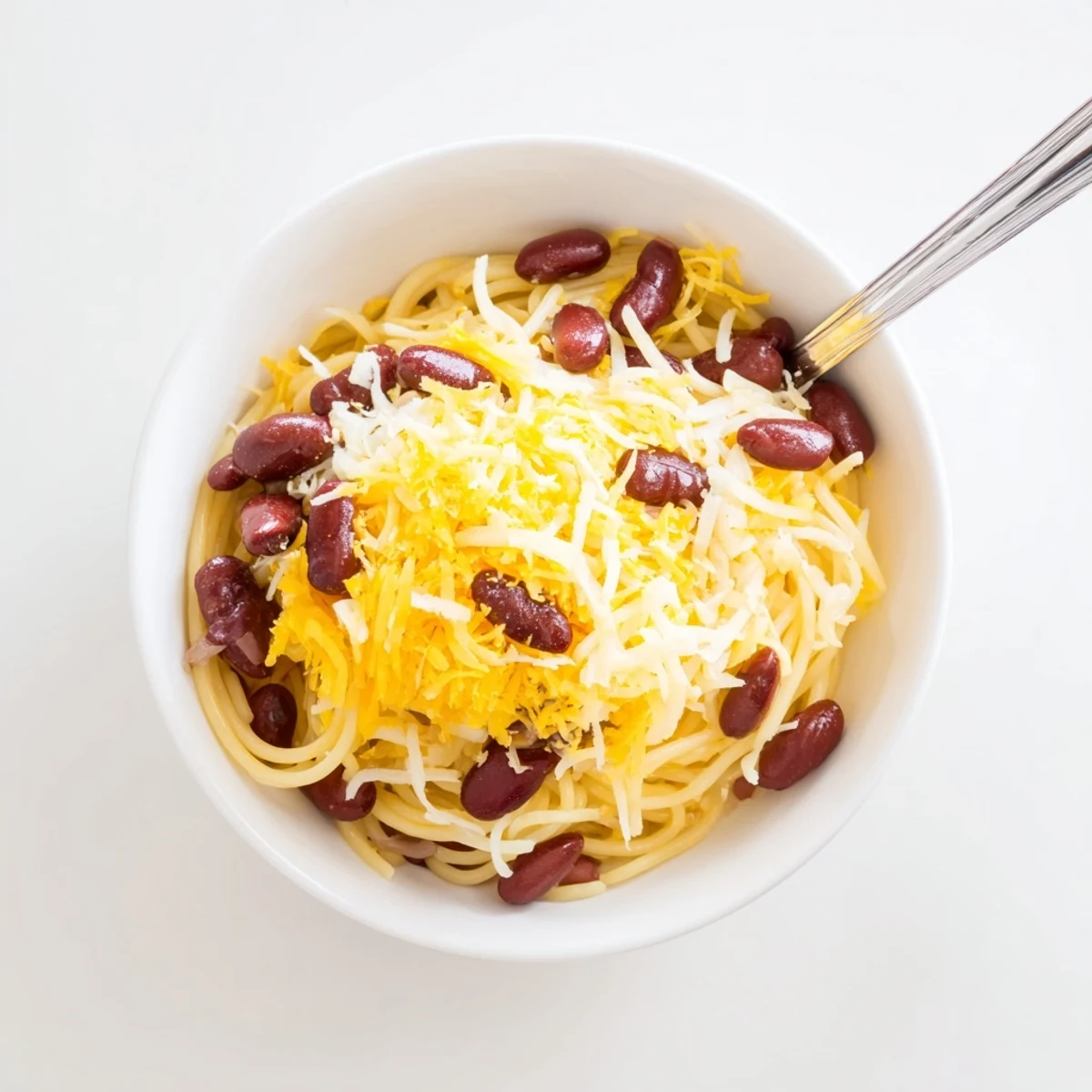 Golden Cincinnati chili ladled over spaghetti with melted cheddar cheese and diced onions