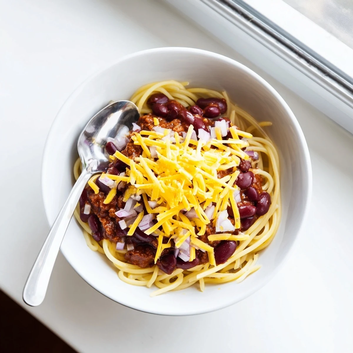 Hearty Cincinnati Chili recipe featuring spiced meat sauce draped over pasta topped with shredded cheddar
