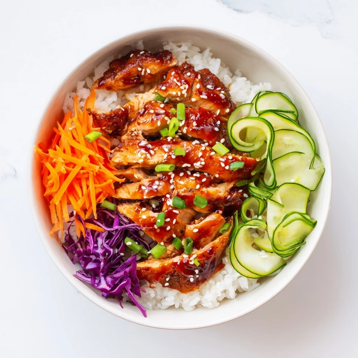 Savory grilled chicken atop a vibrant rice bowl with shredded carrots and cucumber slices