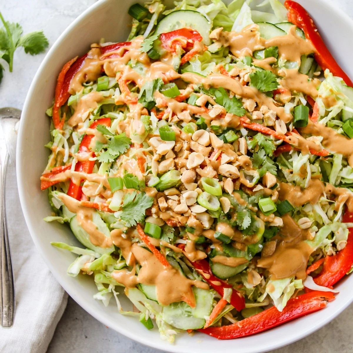 Colorful Thai salad with shredded vegetables coated in creamy peanut sauce and topped with roasted peanuts