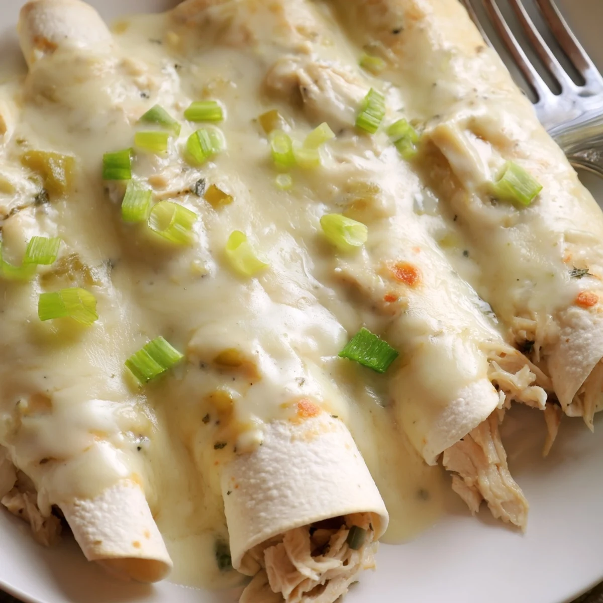 Creamy White Chicken Enchiladas nestled in baking dish, creamy sauce and melted cheese