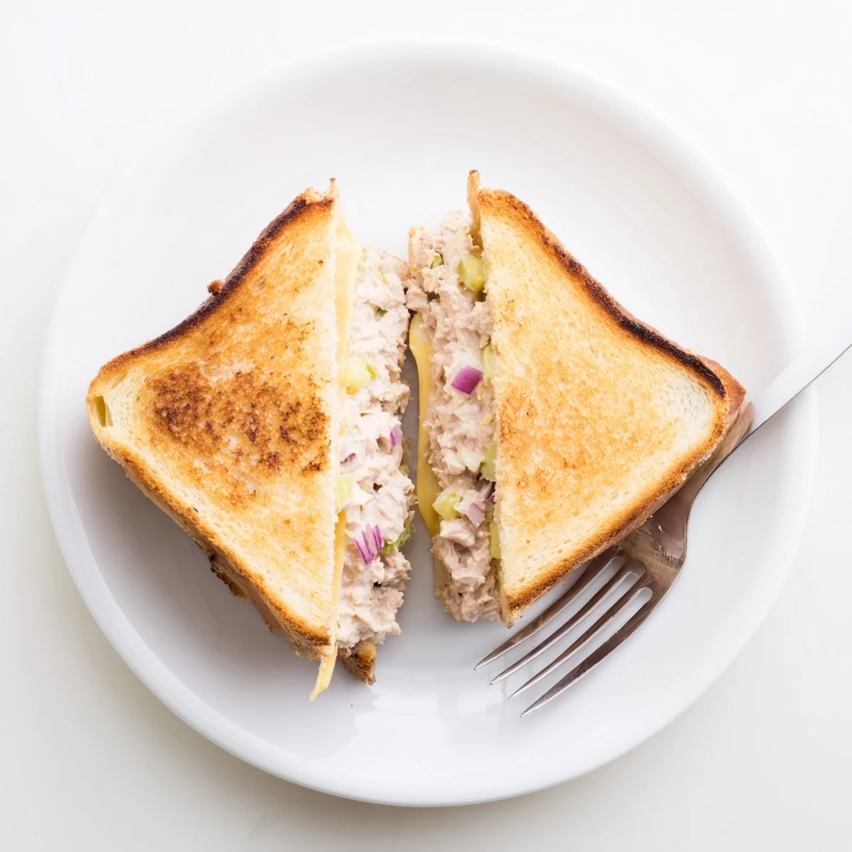 Crispy buttered bread tuna melt sliced in half revealing warm cheesy tuna filling