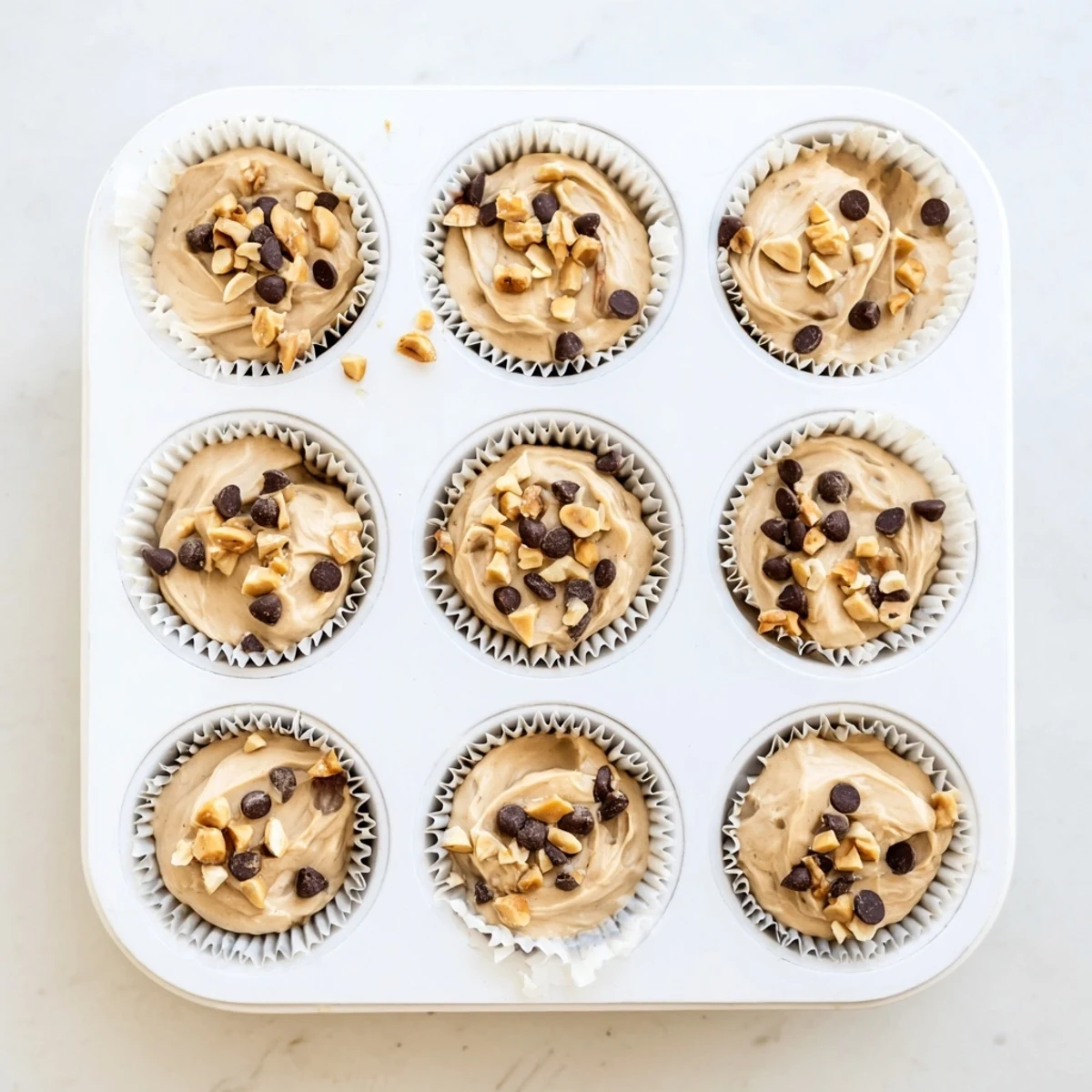 Frozen peanut butter Greek yogurt bites arranged on a white plate topped with melted chocolate chips and chopped roasted peanuts