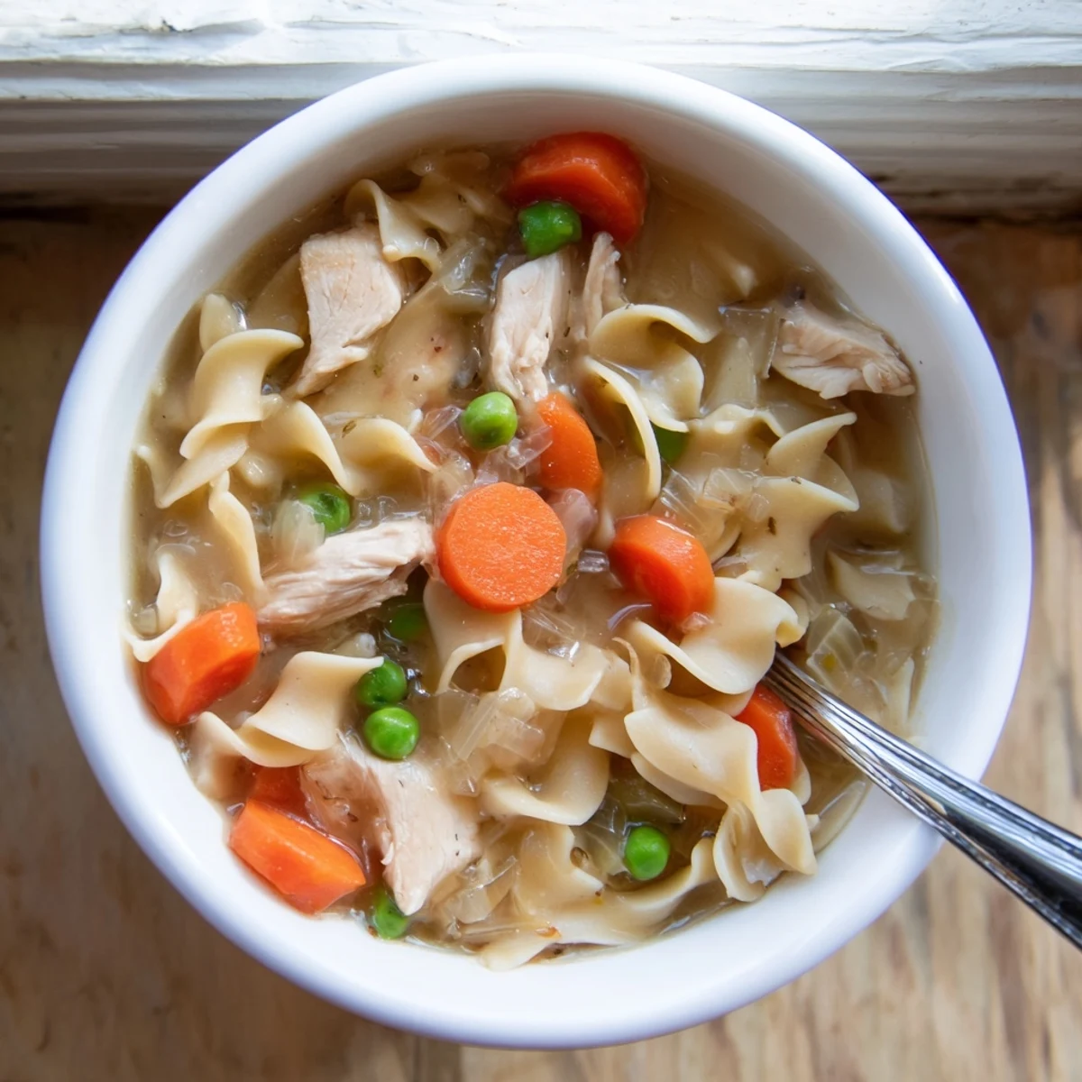 Hearty one pot chicken and noodles steaming in a bowl with vibrant peas and herbs, ready for a cozy family dinner