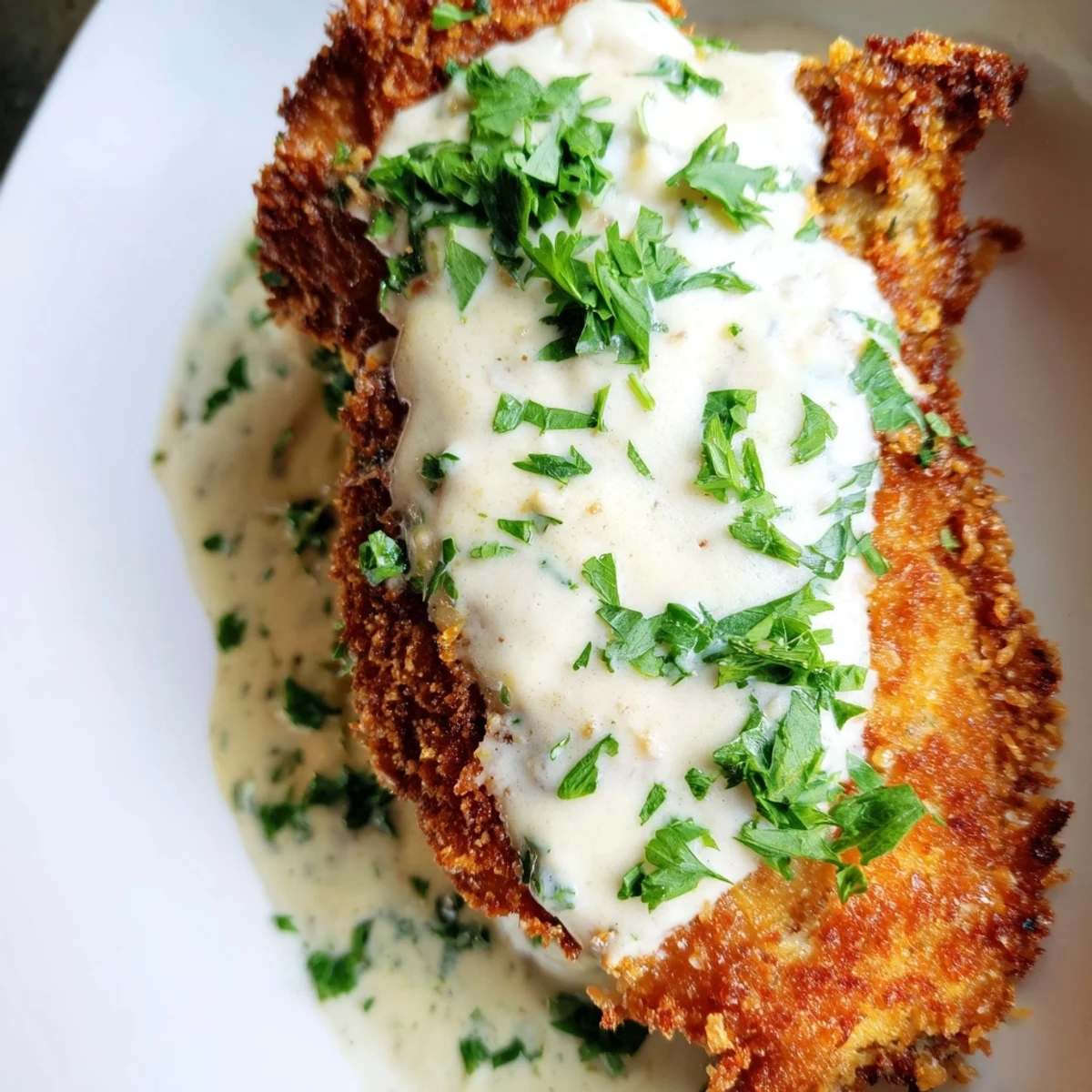Fried crispy chicken topped with smooth garlic cream sauce and fresh green parsley garnish