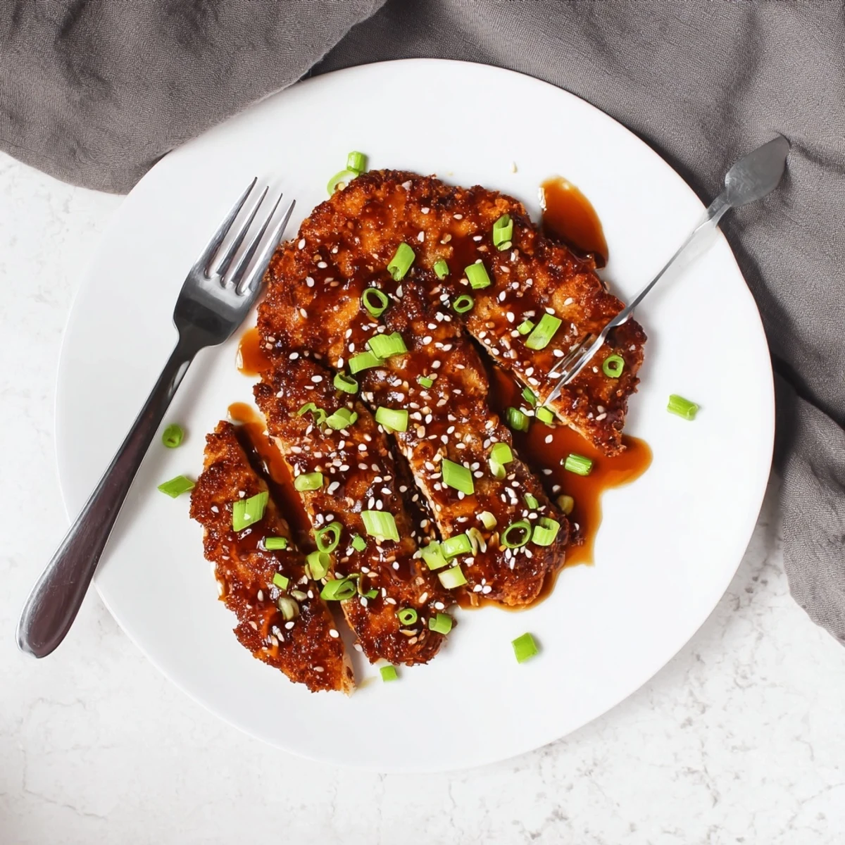 Crispy double-breaded chicken cutlets coated in thick honey garlic glaze, served on a white plate with sesame seed topping