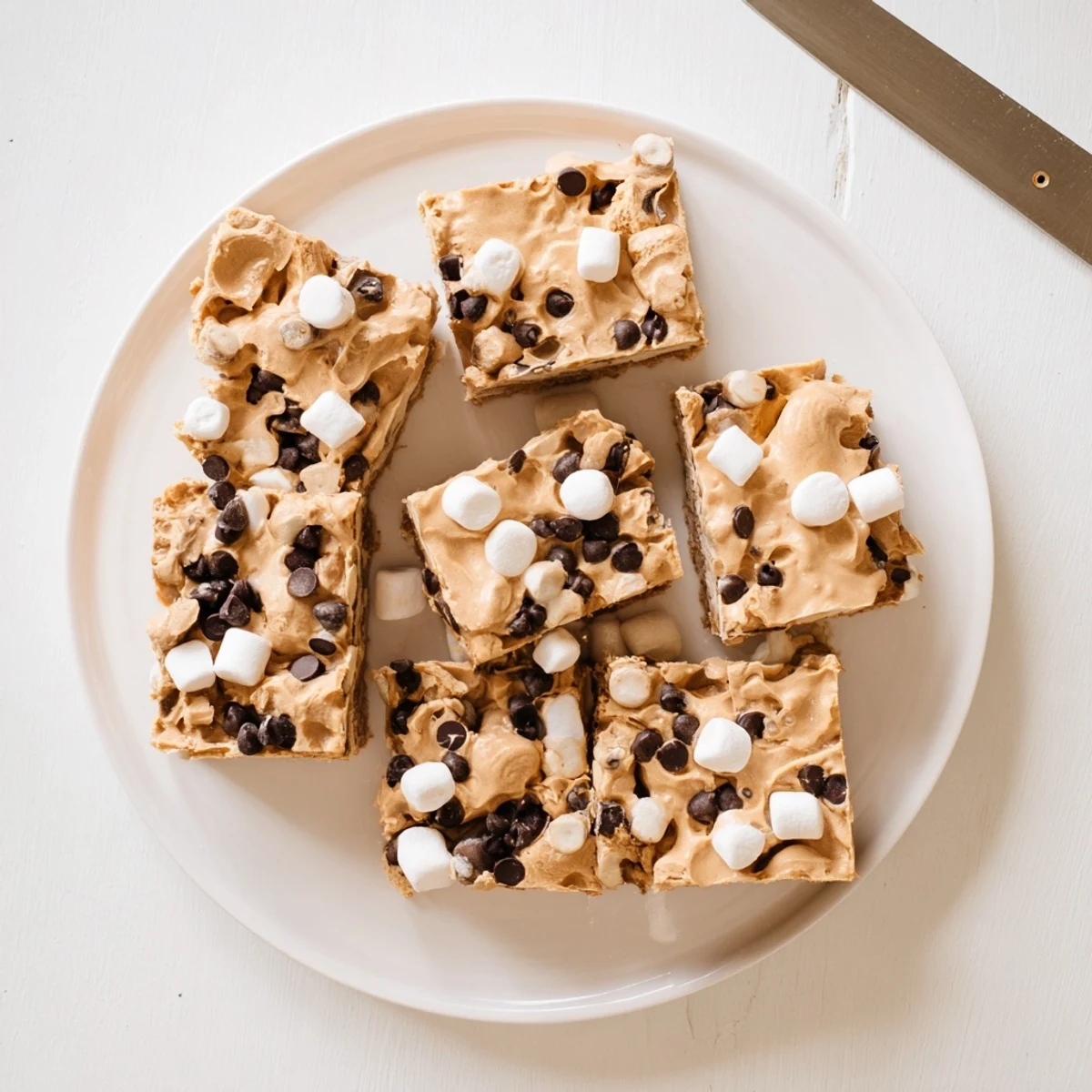 Golden gluten free peanut butter marshmallow squares studded with fluffy white mini marshmallows on a white serving plate