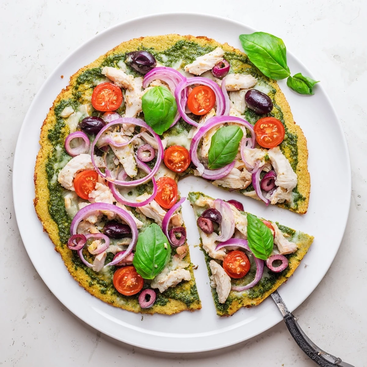 Healthy gluten-free chicken pesto pizza with juicy chicken breast, vibrant green pesto sauce, and red onion on a golden almond flour crust